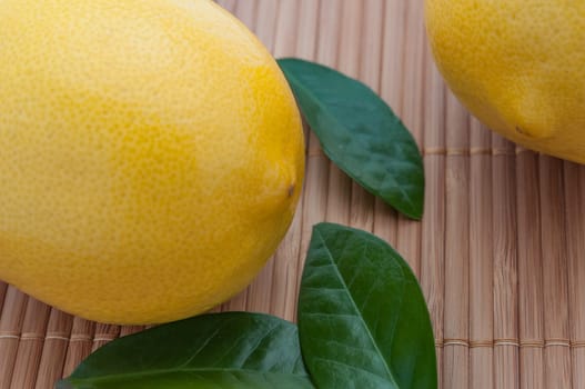 Close-up of large lemons and green leaves on bamboo mat.
