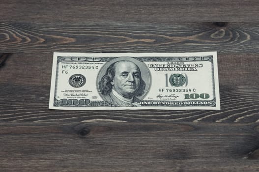 One hundred US dollars. One bill on a wooden table. Frontal side.