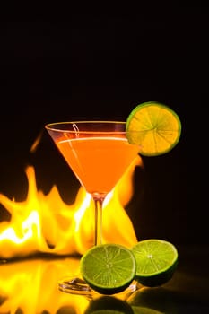 colorful orange cocktail in nice carroty color to front of a black background and fire