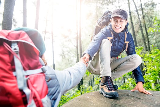 Portrait of asian traveler man helping woman climbing up on the forest