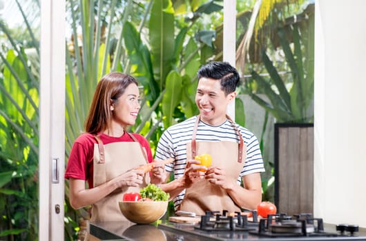 Happy asian couple preparing fresh vegetables for cooking on kitchen