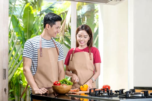 Young asian couple with apron cooking together on the kitchen