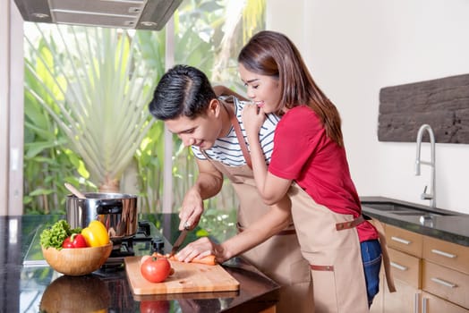 Young asian couple cooking on the kitchen. Male is cutting vegetables
