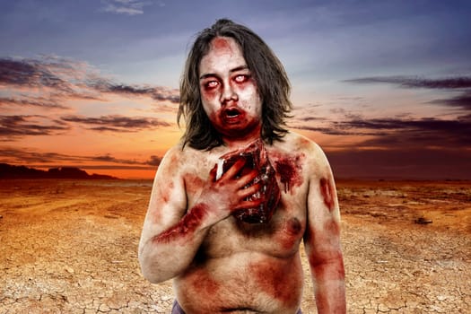 Terrible zombie man with blood eating raw meat on the dry land