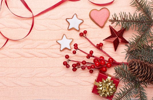 Christmas decor with fir tree branches, gingerbreads and gift box on a pink woolen background with copy space for text. Top view. For greeting card.