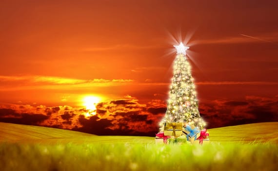 Conceptual decorated shiny Christmas tree on green landscape over cloudy red sunset sky