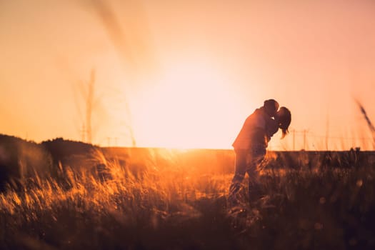 Romantic couple standing and kissing on background summer meadow sunset