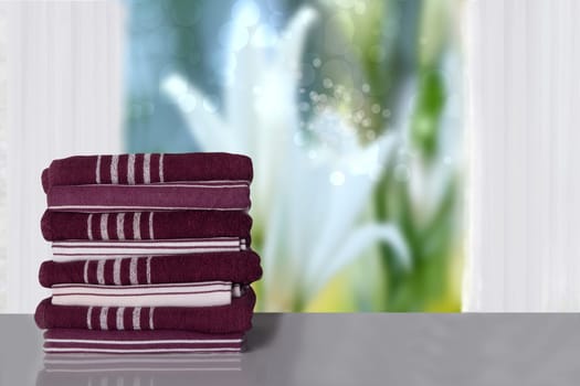 Closeup a stack or pile of striped towels on bright table in front of window with blurred natural summer background. Template for your display product montage. Space.