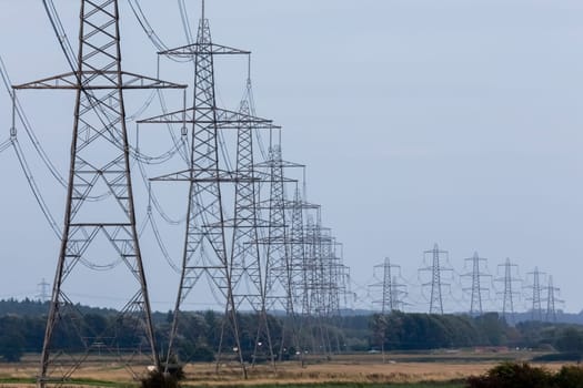 Electricity pylons or transmission towers carrying high voltage power lines and overhead cables above land as part of the national grid network supplying power to peoples homes and businesses