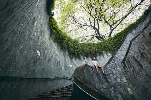 Lonely man sitting on the spiral staircase from underground walkway in Singapore.