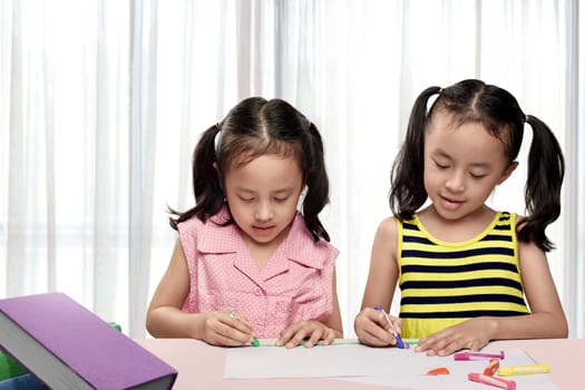 Two asian girl drawing with colorful crayon on paper at home
