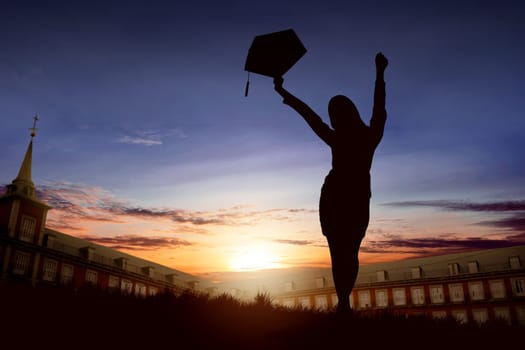 Silhouette of excited woman with graduation hat celebrating graduation on the campus