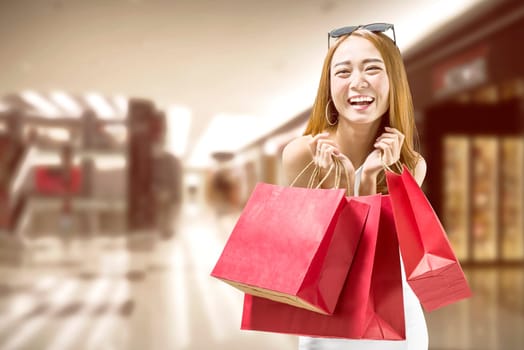 Pretty asian woman with red paper bags on the mall. Black friday concept