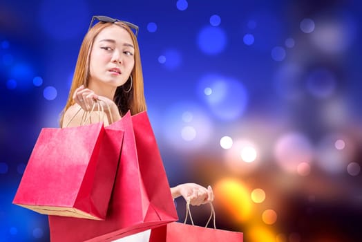 Cheerful asian woman holding shopping bags against blurred lights background. Black friday concept
