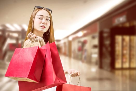 Beautiful asian woman holding red paper bags in mall. Black friday concept
