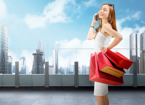 Attractive asian woman using mobile phone while carrying shopping bags at mall balcony