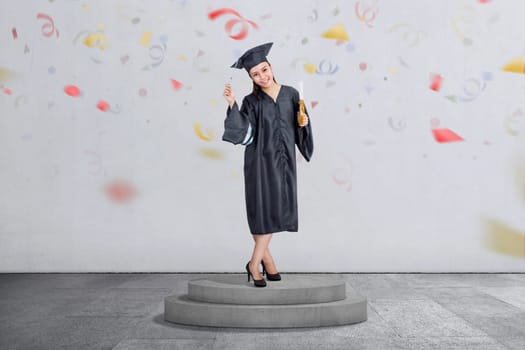 Beautiful asian woman celebrate her graduation with cap and diploma scroll over conffeti background