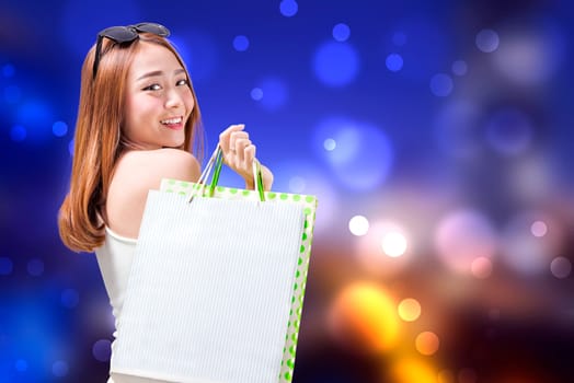 Young asian girl carrying some shopping bags with blurred lights background. Black friday concept