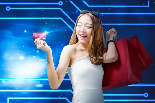 Pretty asian woman with shopping bags showing her credit card against digital blue background