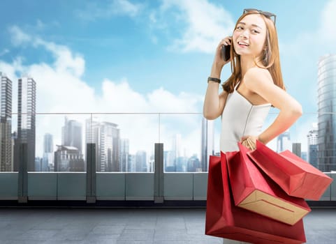 Attractive asian woman with phone holding shopping bags on terrace. Black friday concept