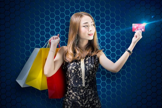Pretty asian woman with shopping bags showing her credit card over digital blue background. Cyber Monday concept