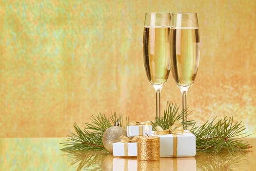 Two glasses with champange, fir tree branch, gift boxes and christmas decorations on a golden background. New year and Christmas.