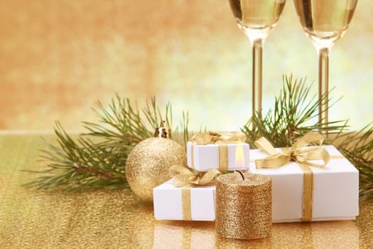 Two glasses with champange, fir tree branch, gift boxes and christmas decorations on a golden background. New year and Christmas.