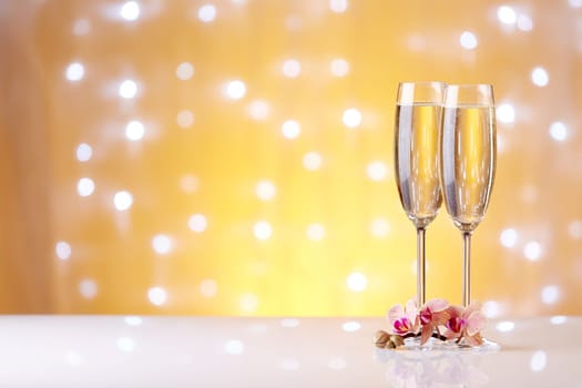 Two glasses with champange and flowers on a yellow background with lights of garland.