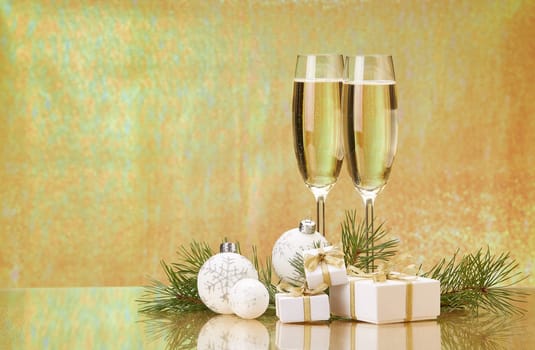 Two glasses with champange, fir tree branch, gift boxes and christmas decorations on a golden background. New year and Christmas.