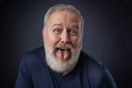 Portrait of an old man making a nasty grimace and pulling the tongue out