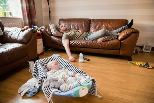 Exhausted father having a nap on the sofa while her newborn child has a sleep.