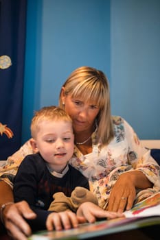 Grandmother and her grandson sitting in bed and reading a story before bedtime. Relaxing and spending some quality time together.