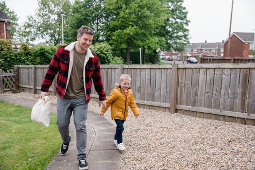 Little boy holding his fathers hand as they walk along the garden path to get back to the house. They are smiling and laughing on the way back.