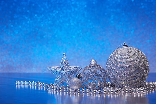 Christmas decoration with silver balls, star, gift box and garlands lying on a blue background. New year and Christmas background with copy space for text. Greeting card.