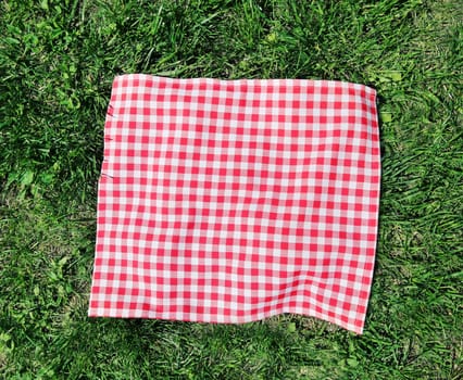 Red checkered picnic cloth over green grass top view.