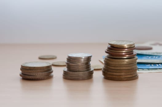 Three stacks of coins and bills lie on the wooden table.