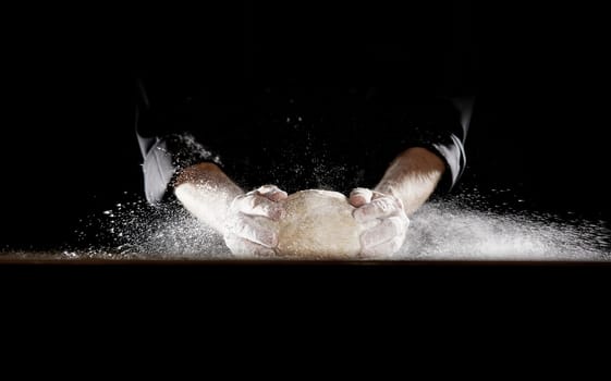Unidentified man in black outfit using his hands slamming dough into table causing flour to fly into the air