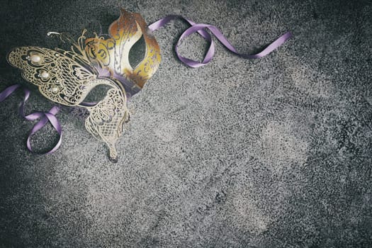 Srylish metallic gold Mardi Gras or carnival mask background on a textured grey background with vignette