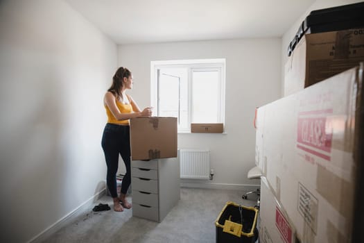 Teenage girl is taking a break from unpacking and is using her smart phone in her new bedroom.