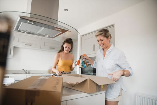 Mature woman and her teenage daughter have moved in to a new home and are unpacking boxes in the kitchen together.