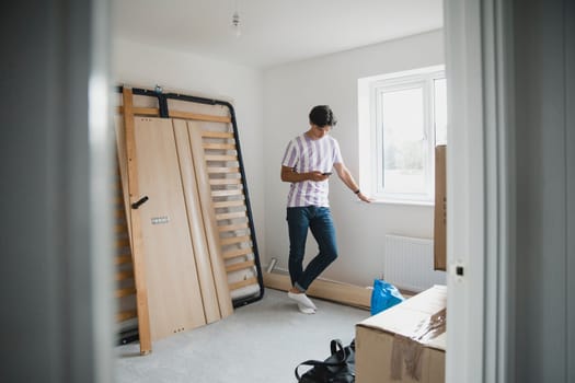 Young man is taking a break from unpacking to use his smart phone.