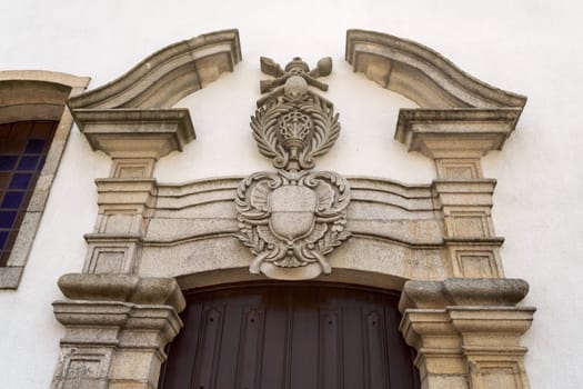 Detail of the lateral portal with a broken pediment and religious coat of arms of the Baroque Church of Mercy in the historic town of Trancoso, Portugal