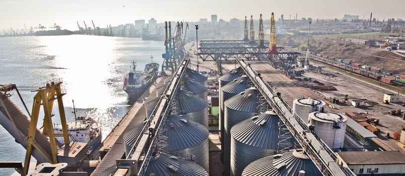 Grain from silos being loaded onto cargo ship on conveyor belt with freight train