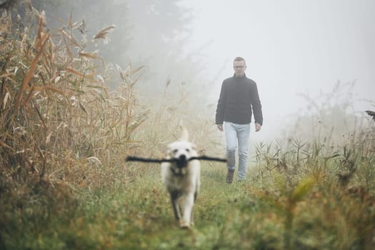 Young man playing with dog (labrador retriever) in autumn foggy morning.