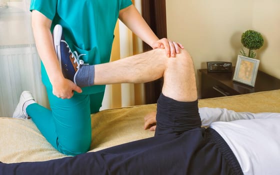 Physiotherapist doing exercises for leg recovery to immobilized male patient at home. People, health and recovery concept.