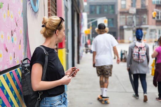 Closeup of female hipster with smart phone. Woman using smartphone against colorful graffiti wall in East Village, New York city, USA.