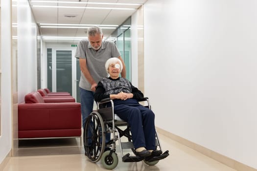 Middle aged man helping and making company to elderly 95 years old woman sitting in the wheelchair. Social aid for retirement citizens concept.