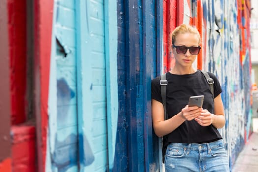 Closeup of female hipster with smart phone. Woman using smartphone against colorful graffiti wall in East Village, New York city, USA.
