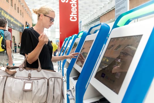 Casual caucasian woman using smart phone application and check-in machine at the airport getting the boarding pass. Modern technology on airport.