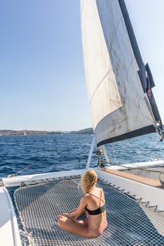 Woman in bikini tanning and relaxing on a summer sailin cruise, sitting on a luxury catamaran near picture perfect Palau town, Sardinia, Italy.